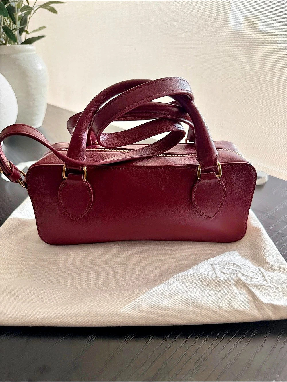 Reformation leather burgundy bag with top handle and long strap.